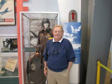 Dennis Earles in front of the glass display case is his father's exhibit showing his fighter pilot status and naval contirbution during the Korean War. 